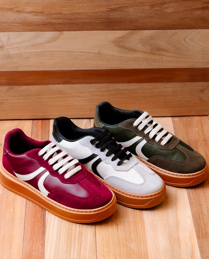 gallery-02 Three pairs of trendy sneakers on a wooden floor offer a stylish footwear display.