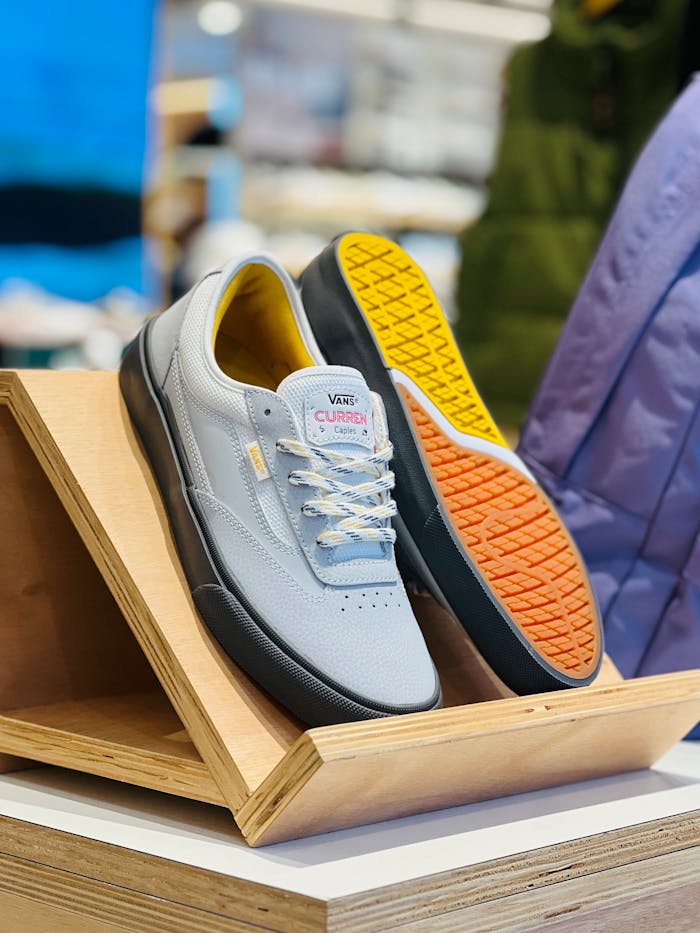 gallery-01 Modern gray sneakers with vibrant soles showcased on a wooden stand in a retail environment.